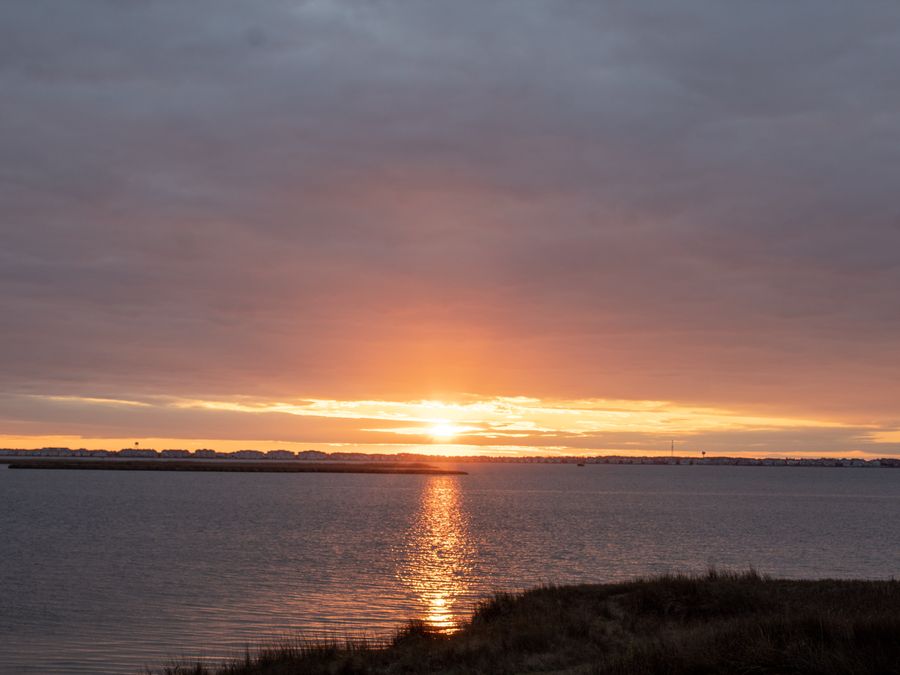 The sun touching a flat water horizon, laying a golden path across the water.